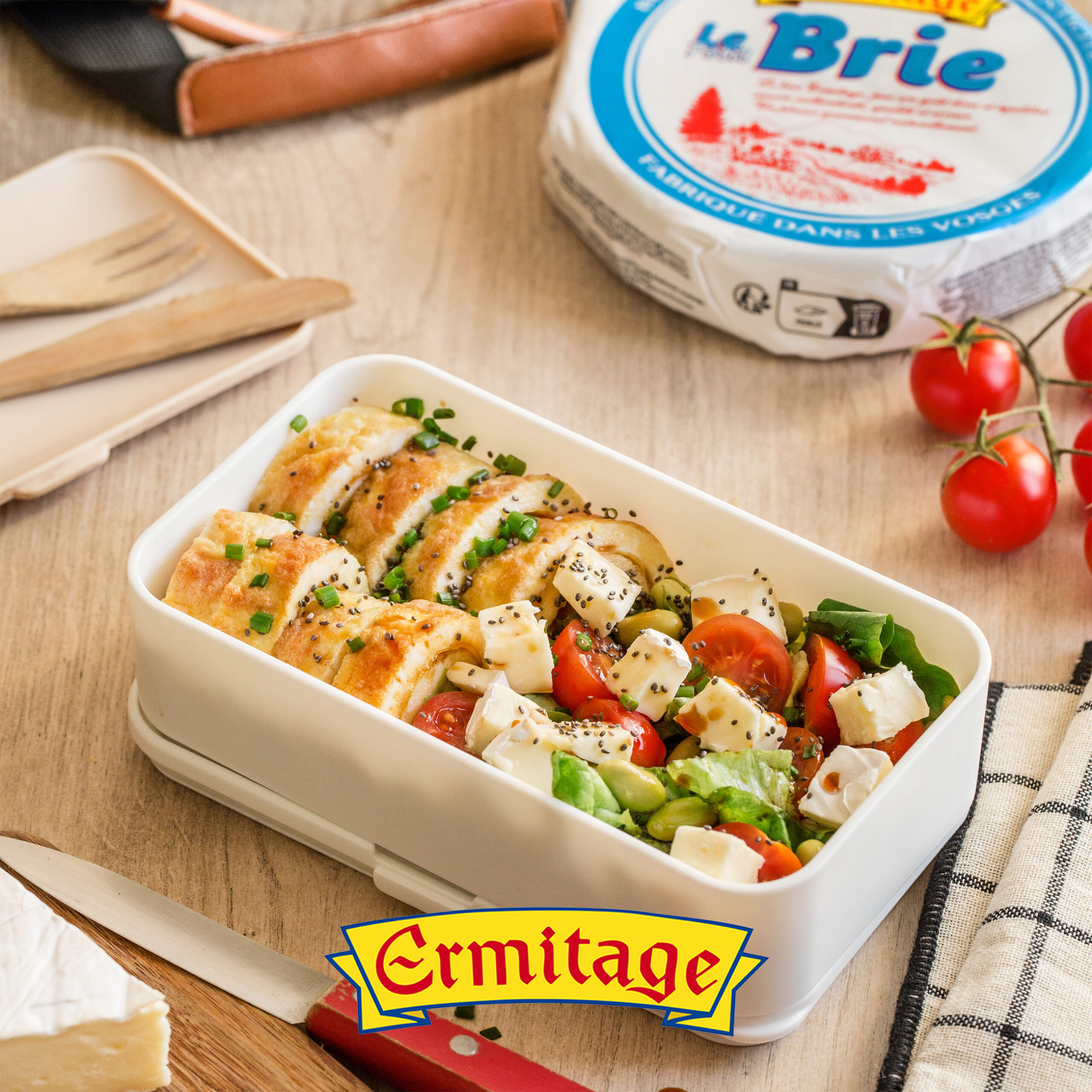 Bento composé de tranches d’omelette roulée aux herbes, Brie, tomates cerises, et salade.