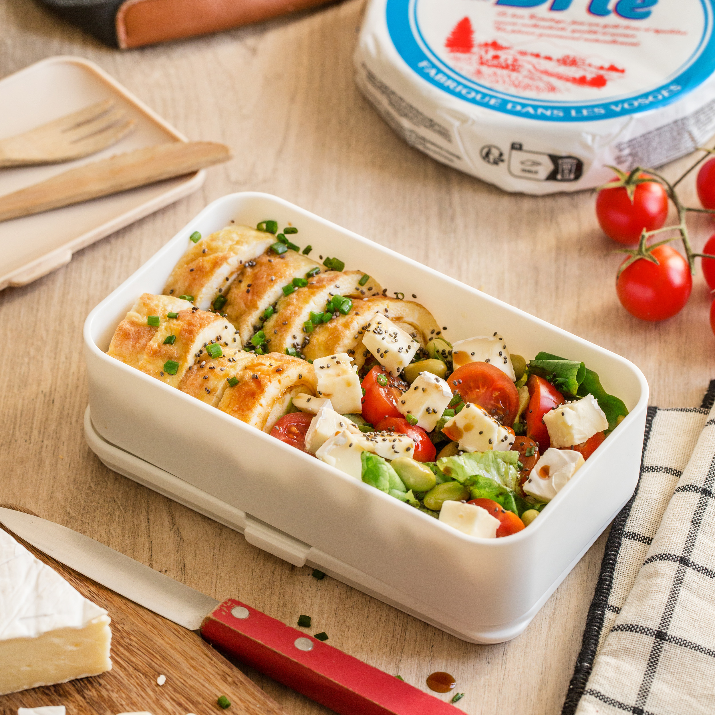 Bento composé de tranches d’omelette roulée aux herbes, Brie, tomates cerises, et salade.