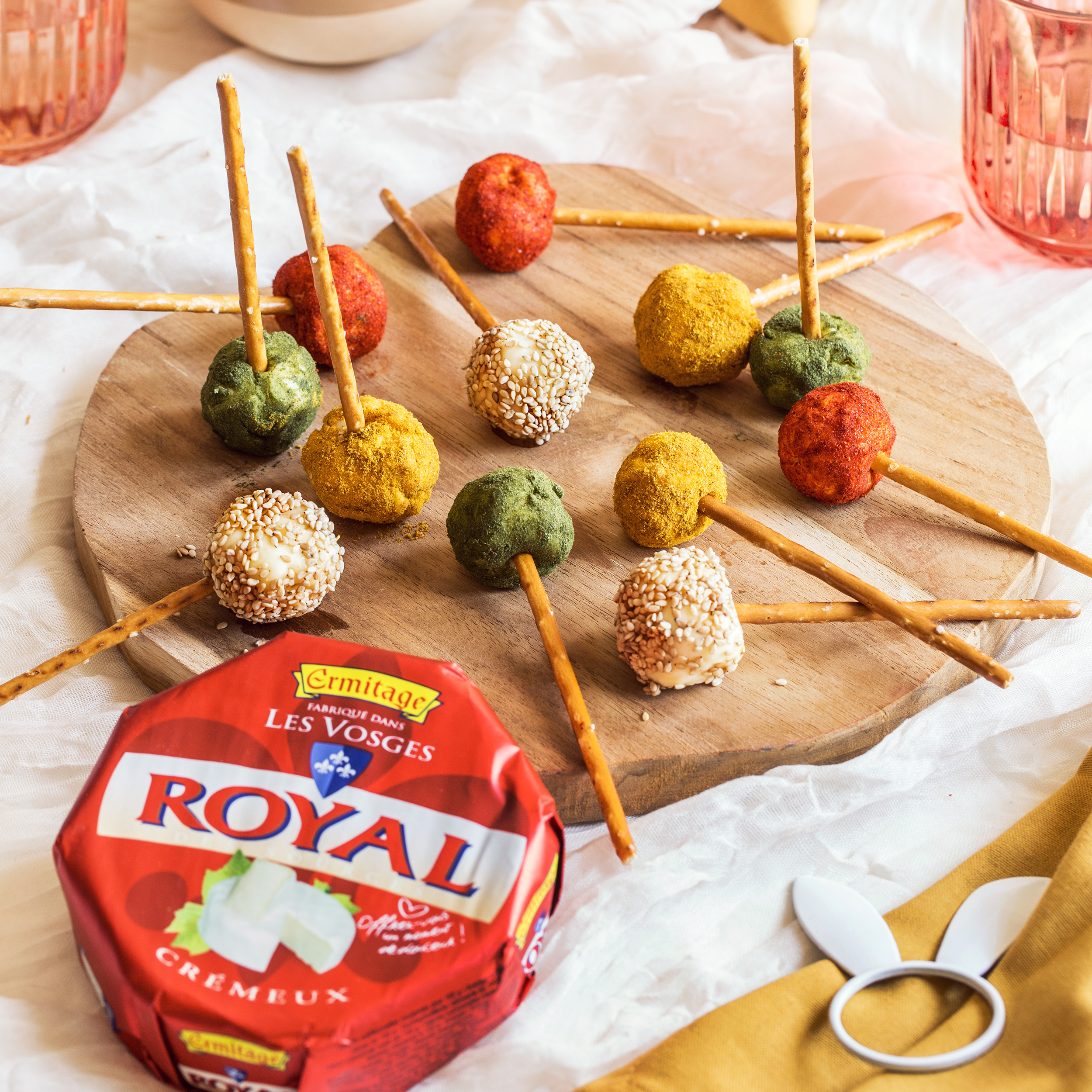 Sucettes apéritives au Royal Crémeux Ermitage, enrobées de toppings colorés (sésame, épices, herbes) avec bâtonnets de bretzel.